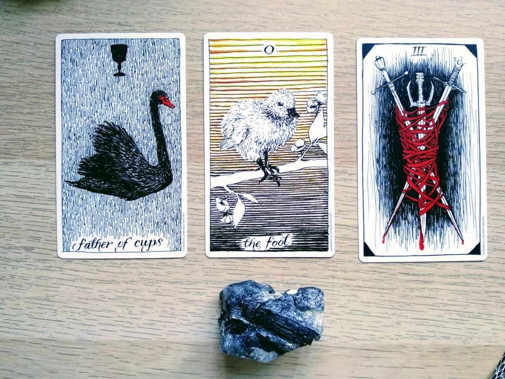 3 cartas: padre de copas, el Loco, y 3 de espadas. En la imagen se ve también un cuarzo turmalinado.