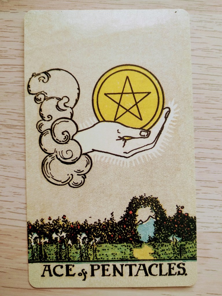 En la imagen hay una carta. Una mano en el cielo tiene un pentáculo (una moneda de oro con una estrella de cinco puntas grabada) en modo de ofrenda. En el suelo hay un jardín con una puerta que lleva a la montaña.